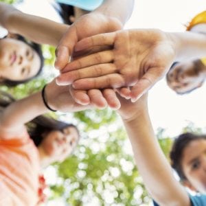 Diverse group of kids put their hands together while playing in the park. Photo shot from low angle point of view. Focus is on the kids' hands.