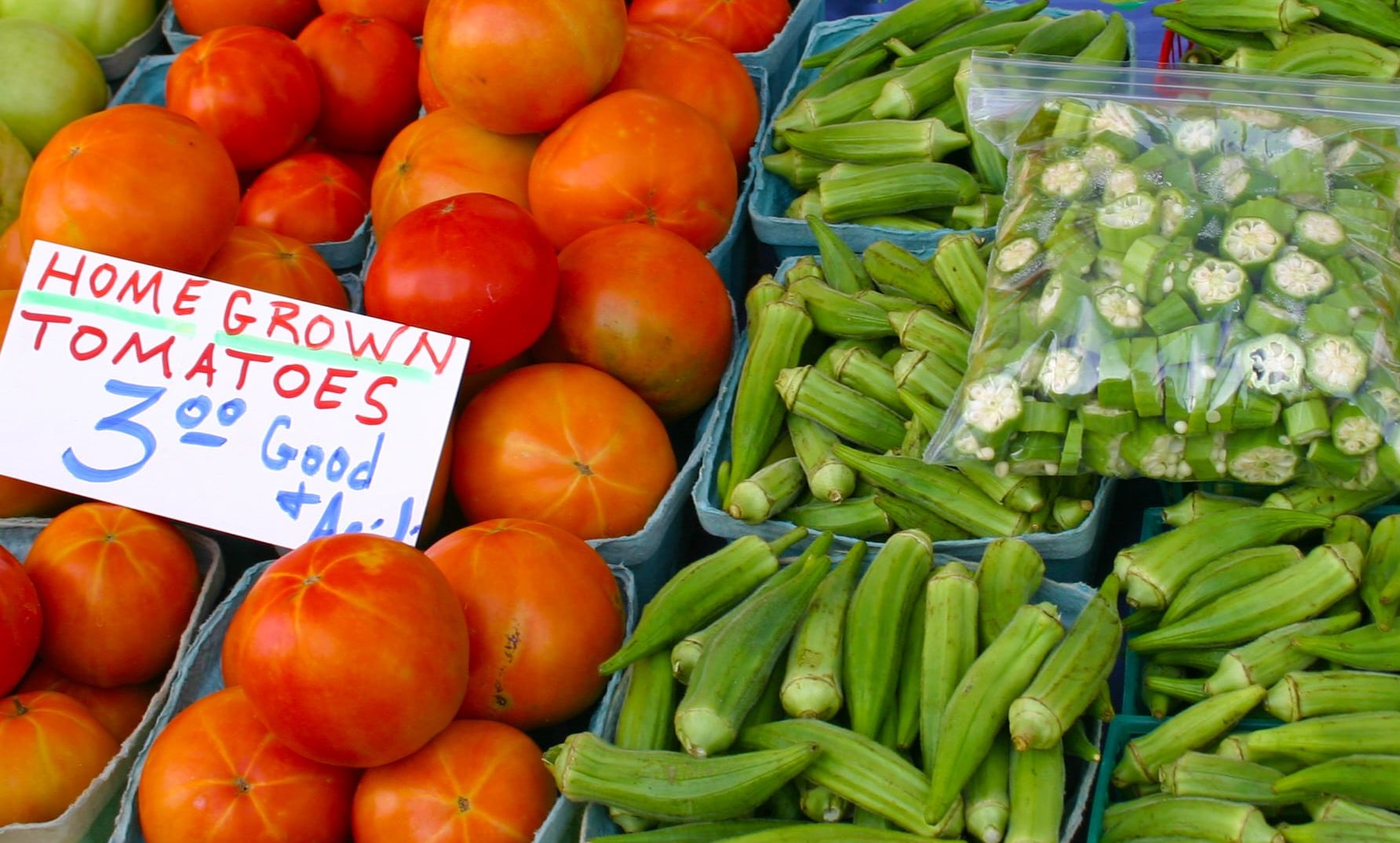 fresh tomatoes and okra in baskets for sale at a fresh vegetable stand