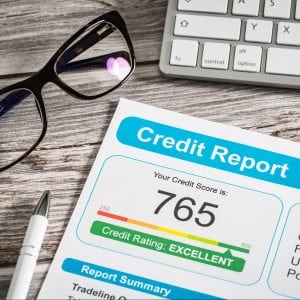 Credit report on a desk beside a pair of glasses and computer keyboard.