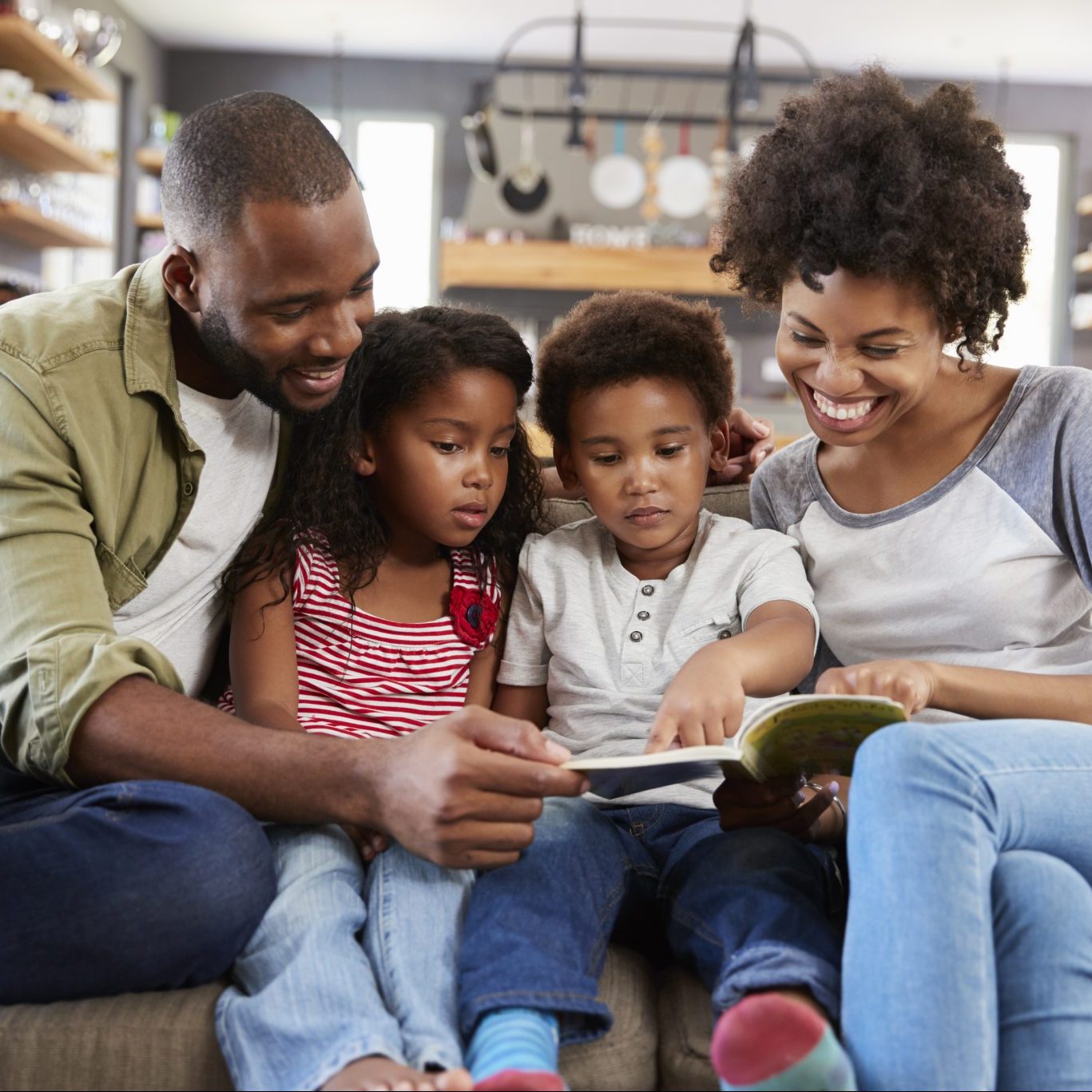 Mom and dad with two young children sitting on sofa reading a book together