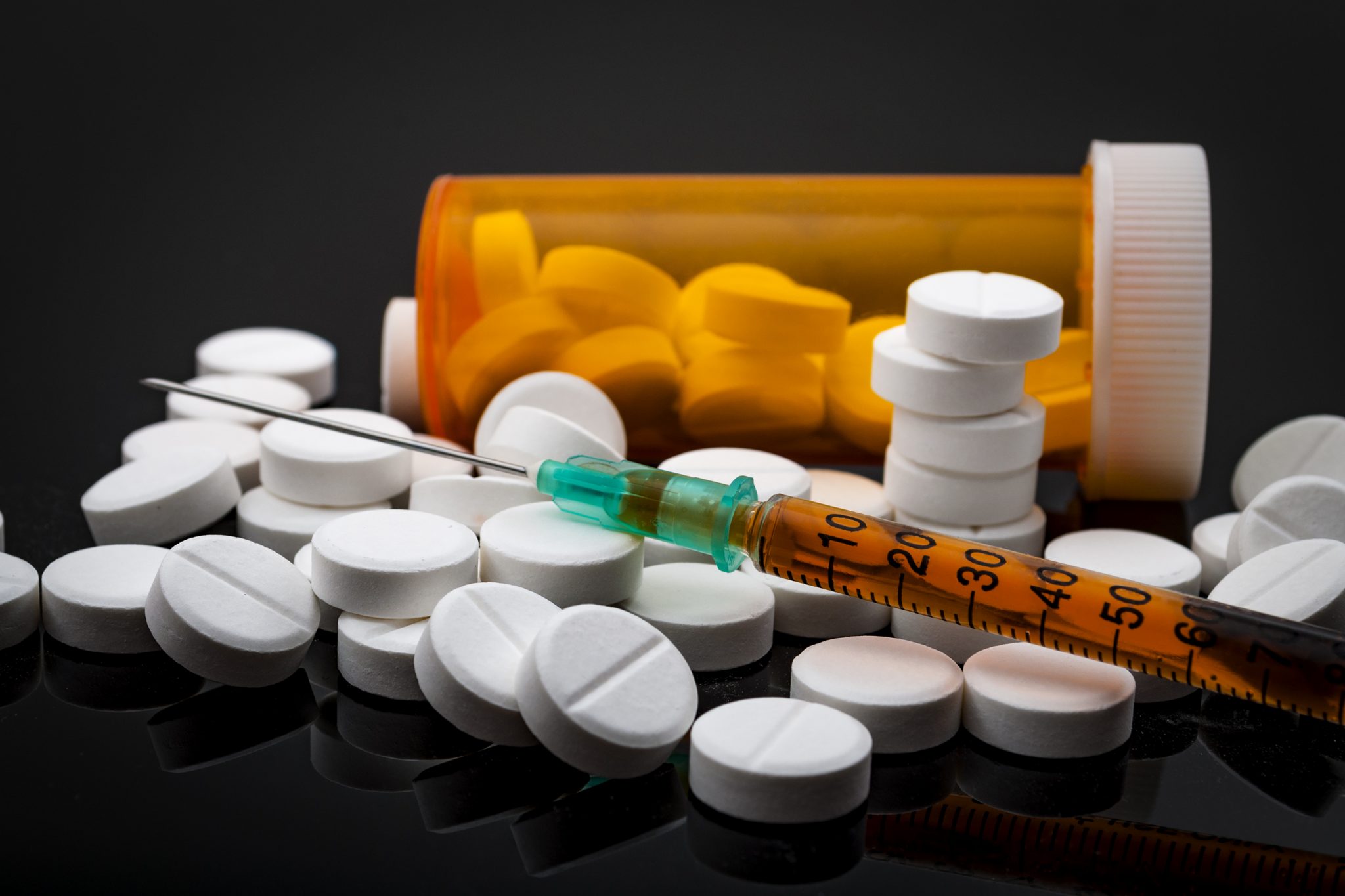 Prescription drug bottle, spilled opioid pills with Syringe