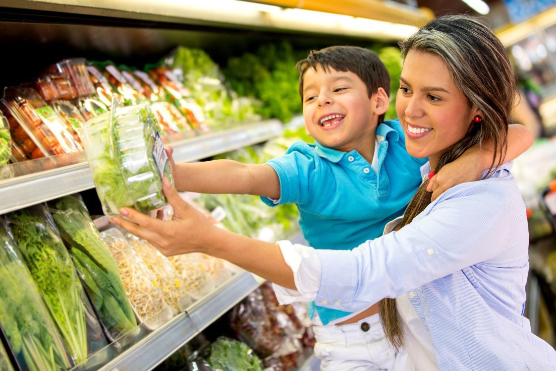 A hispanic mother and her son in the produce section of a grocery store.