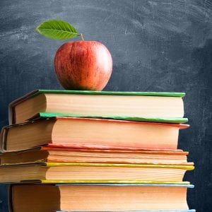 School accessories, books and fresh apple against chalkboard