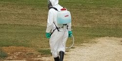 ully protected Applicator with spray backpack walking in a field.