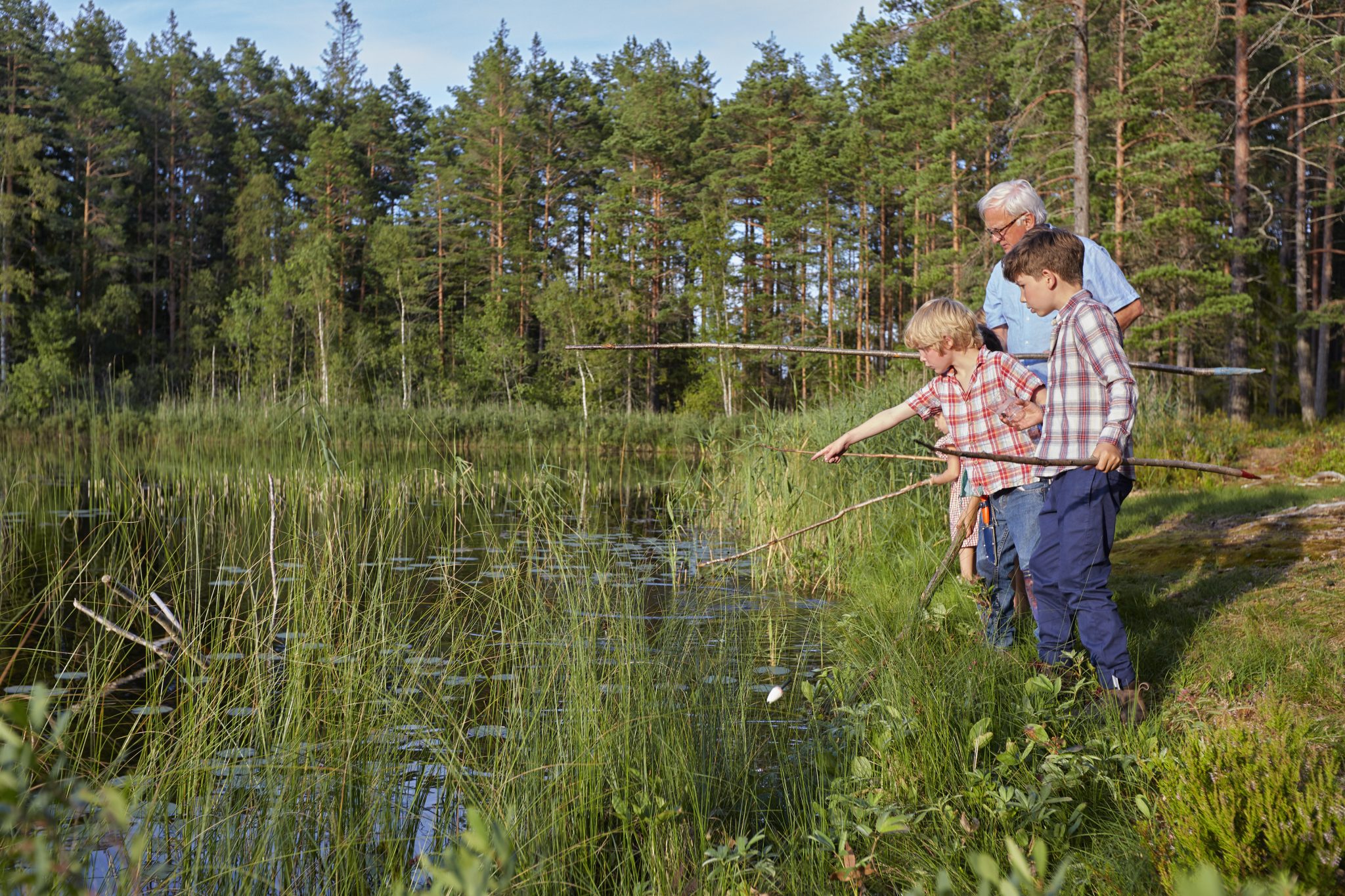 Grandfather teaching grandsons fishing at sunny lakeside