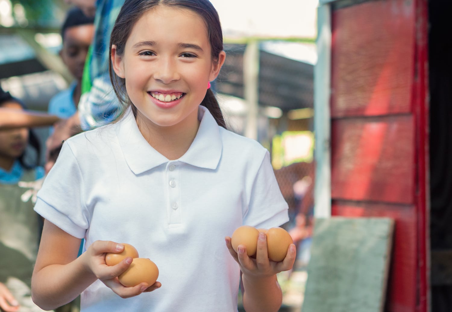 A young girl in a white collard shirt holding two eggs in each hand.