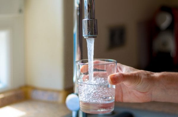 Woman filling a glass of water from a stainless steel or chrome tap or faucet, close up on her hand and the glass with running water and air bubbles.