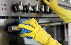 Someone wearing yellow rubber gloves, cleaning the outside of an oven.
