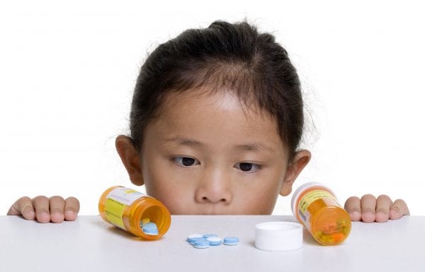 A young girl looks at a pile of pills that was left on a counter.