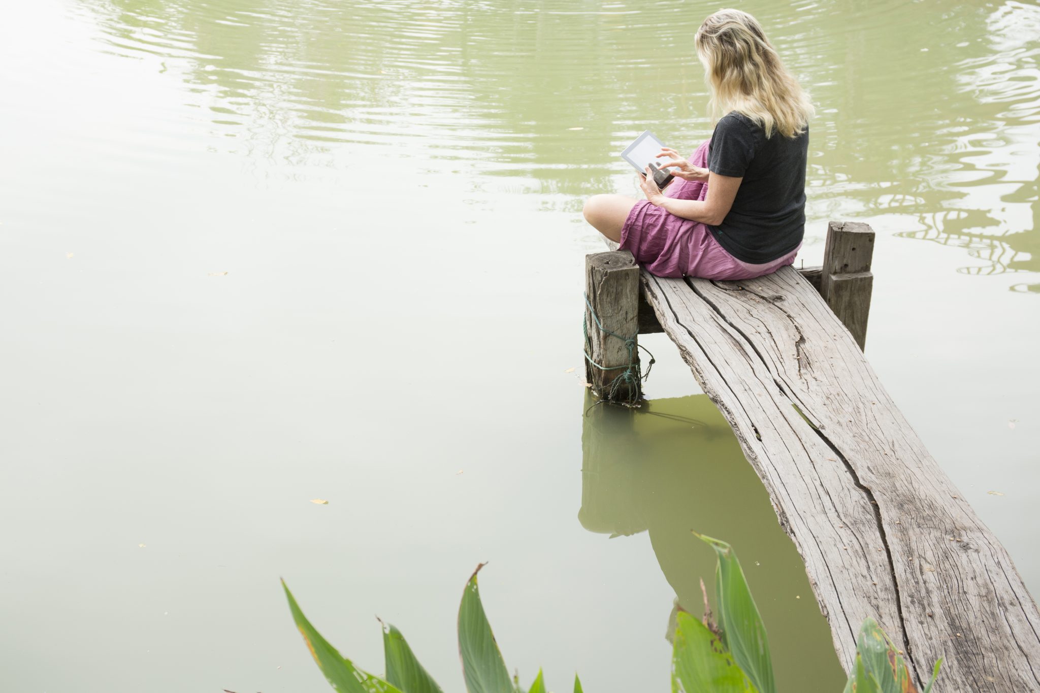 Woman sitting on dock and using digital tablet
