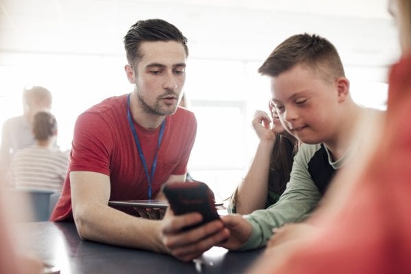 Point of view angle of teacher assisting down syndrome boy with using the smart phone.