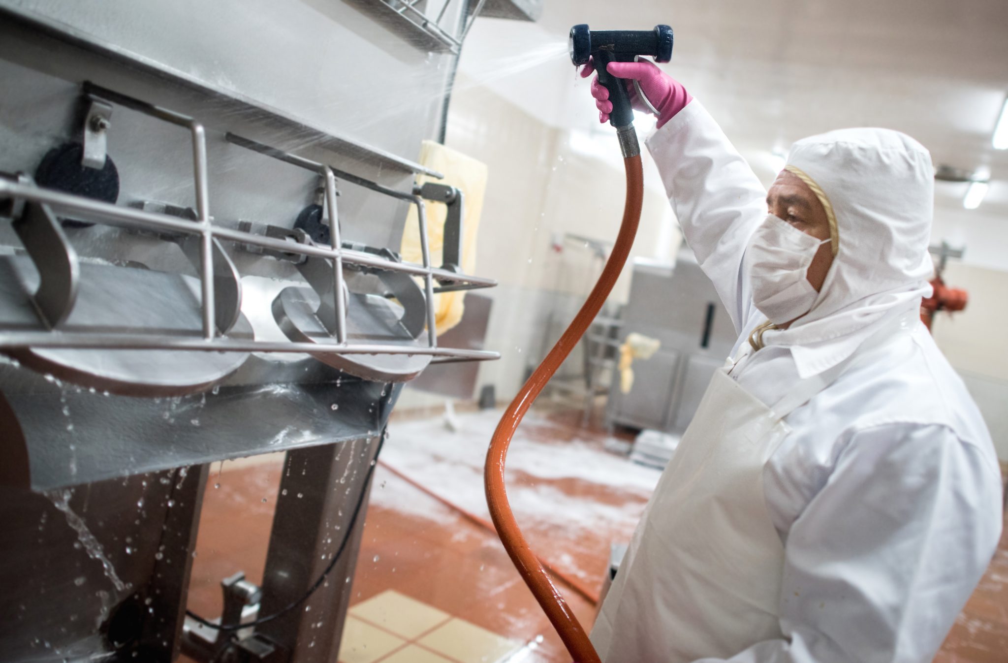 Man washing machines at a factory with a hose