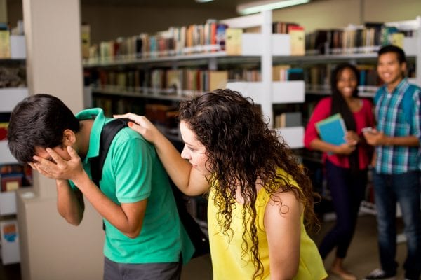 A latin female student helping his sad friend at the library.