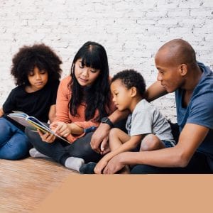 African American parents reading a fairy tale fable story for kids at home. Happy family sitting on the floor indoors