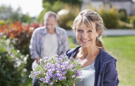 Portrait of smiling woman holding potted flower in garden