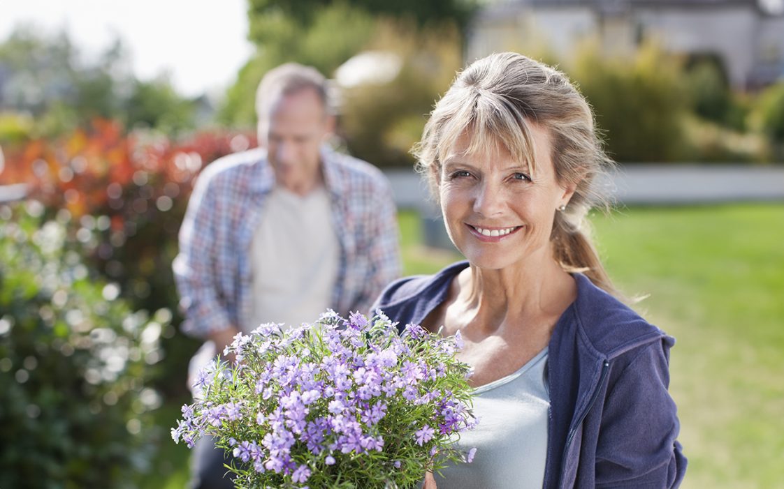 Portrait of smiling woman holding potted flower in garden