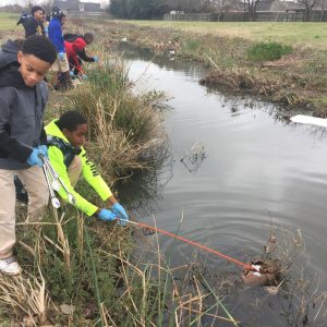 Students line the banks of a drainage stream gathering trash from the water