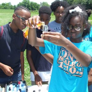 A group of students participating in water chemistry observations. A girl holds a tube of water as she pours in a solution