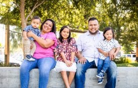 Latino family with young children sits outside in the park.