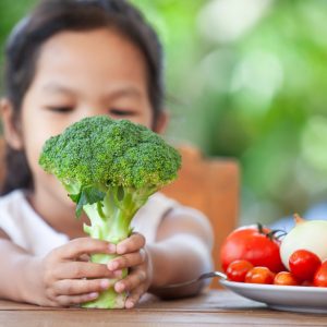 Cute asian child girl holding broccoli and learning about vegetables