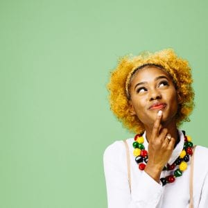 Young African American woman thinking and looking up, isolated on green studio background