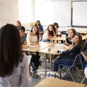 Instructor stands in front of high school student class teaching a lesson.