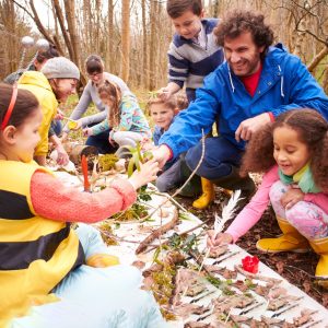 Group of elementary children gather things found in nature to study with two teachers.