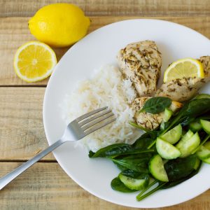 Green spinach and cucumber salad, white rice and chicken fillet baked with thyme and lemon and served on a white plate. Top view
