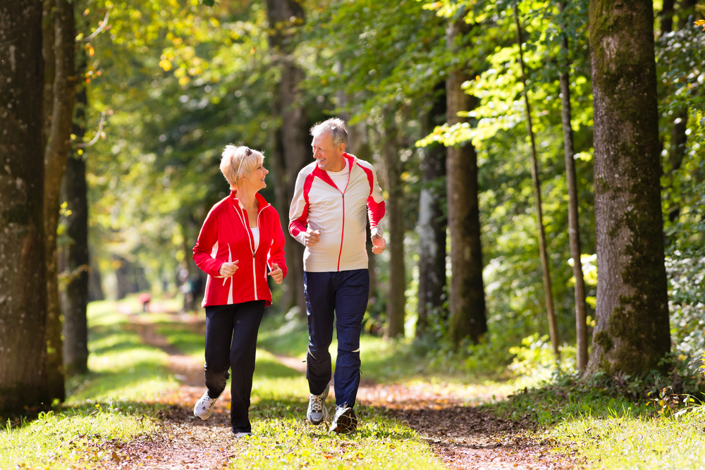 An older couple exercising in a wooded area.