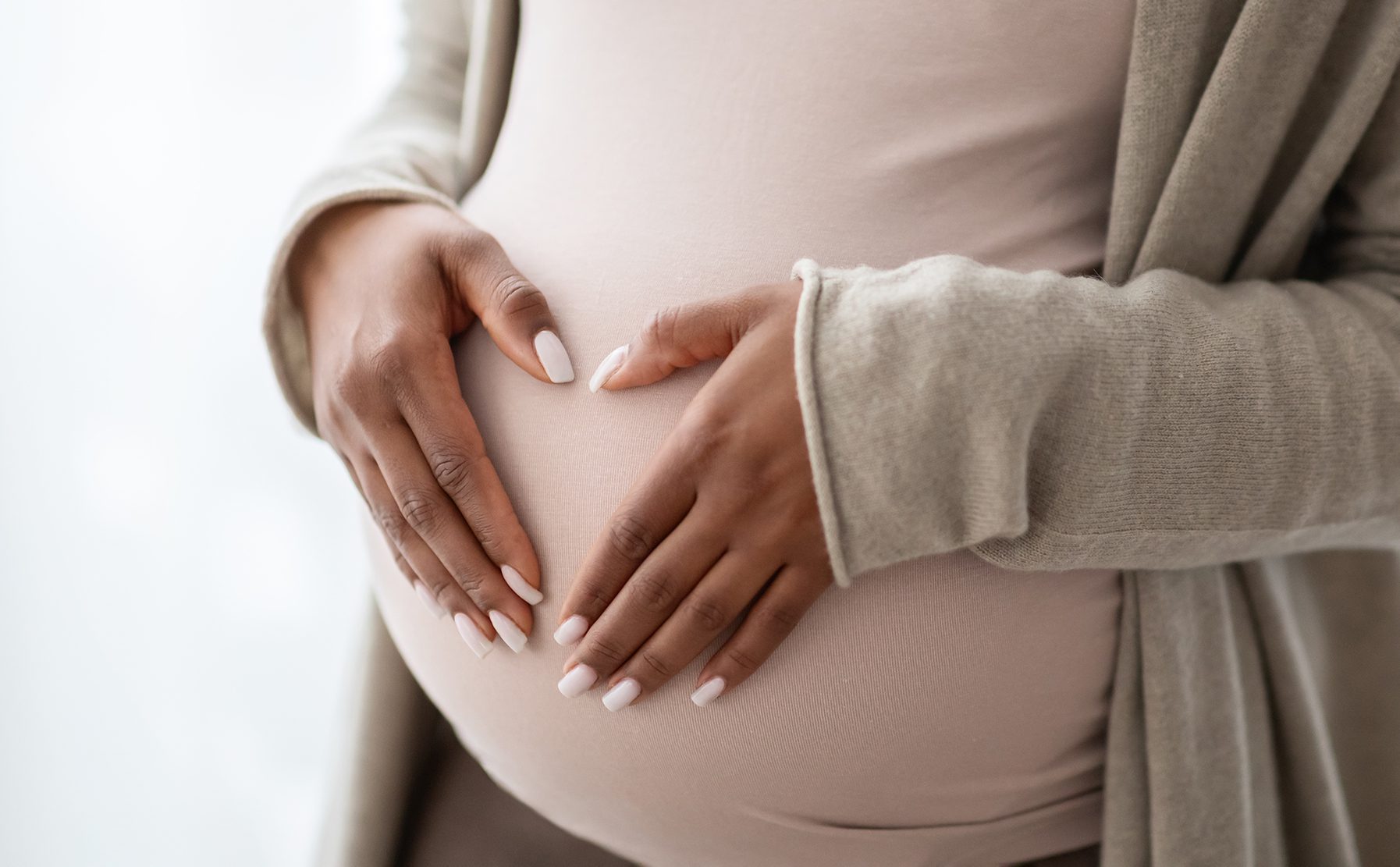 Pregnant Black woman holding palms in heart shape on her stomach.