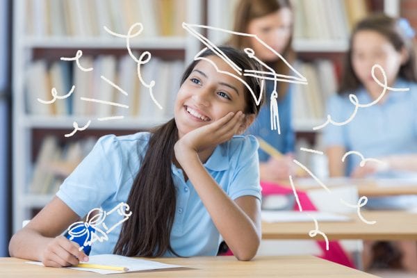 Pretty middle school girl smiles while daydreaming about her future. She is sitting in a class room.