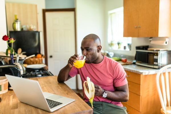 African American man eating a banana and drinking orange juice.