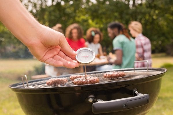 Man using meat thermometer while barbecuing on a sunny day