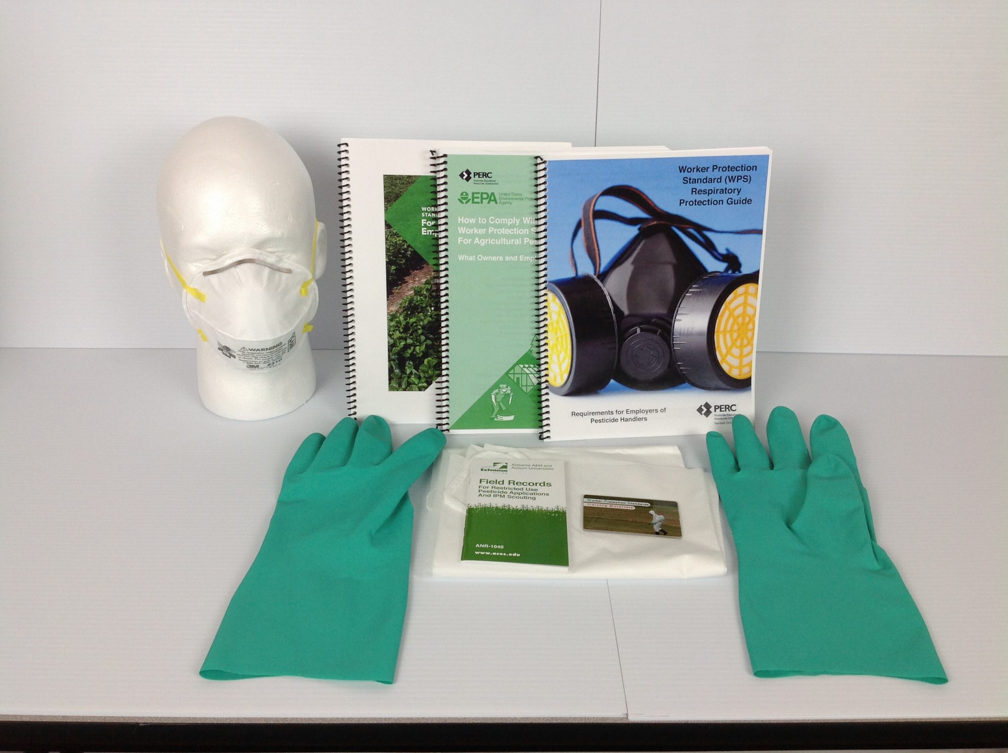 Image of training manuals, green gloves, face mask and other documents.