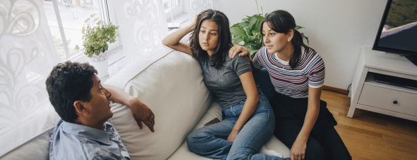 Daughters listening to father while sitting on sofa at home