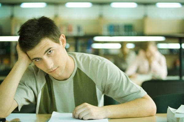 Male student studying in library, looking at camera