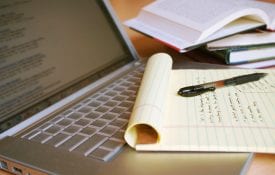 Laptop computer with books, pen and yellow legal pad