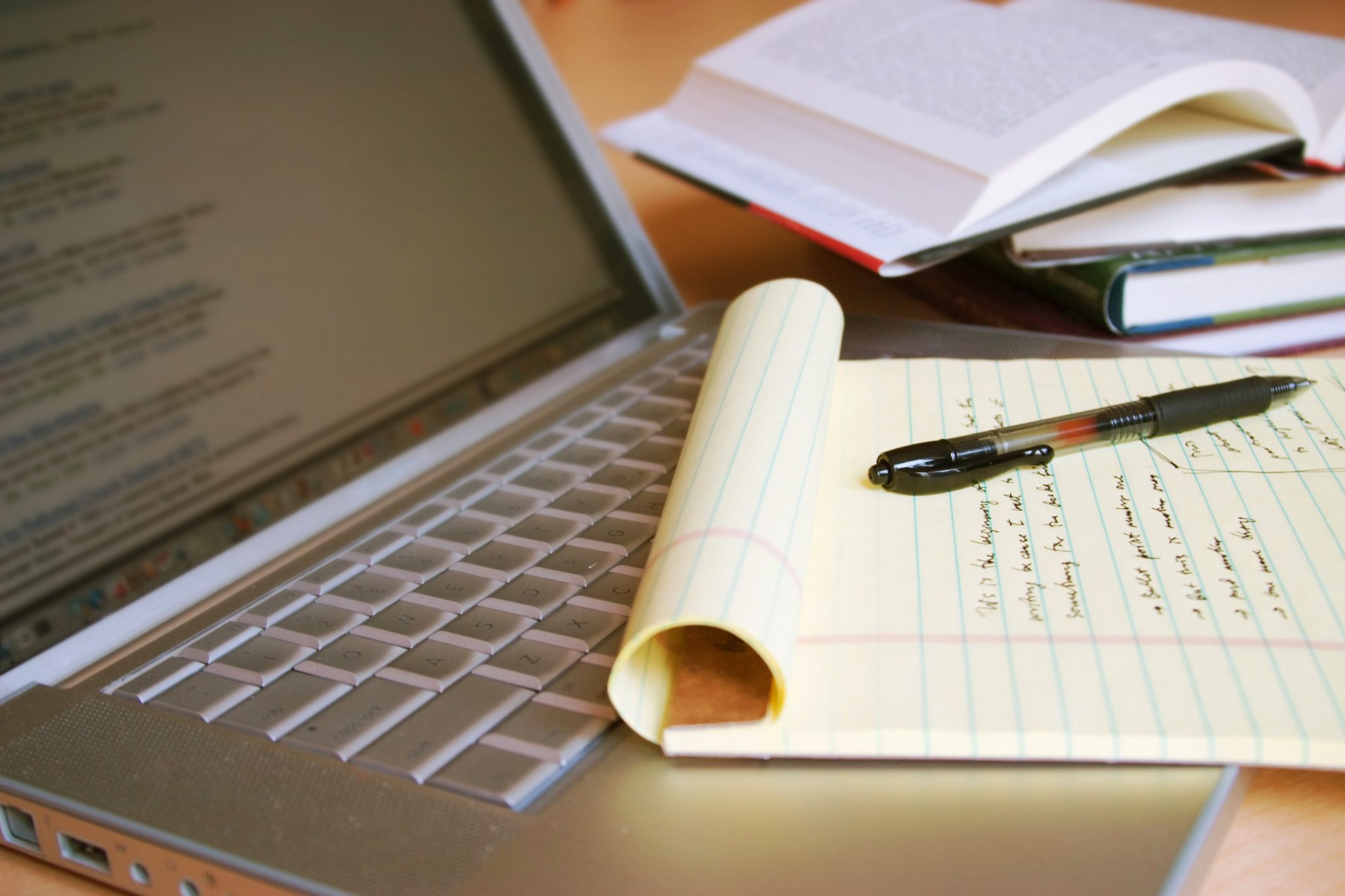 Laptop computer with books, pen and yellow legal pad