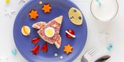 rocket or space shuttle shaped sandwich with cheese and salami decorated with stars, moon and planets on a blue plate