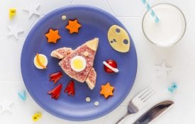 rocket or space shuttle shaped sandwich with cheese and salami decorated with stars, moon and planets on a blue plate