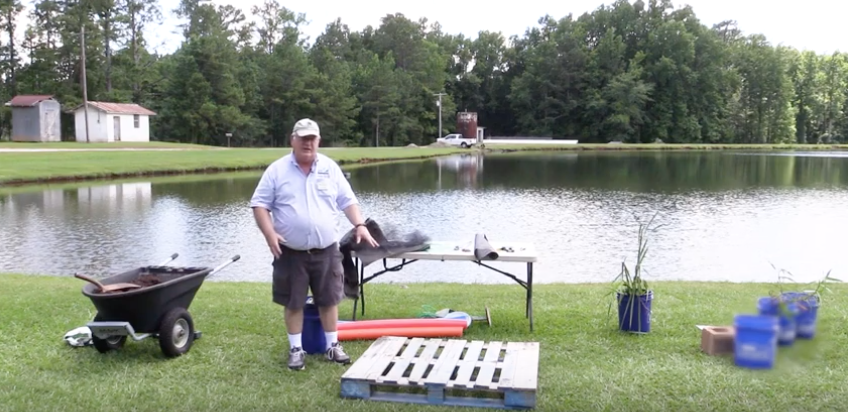 A man standing near a pond building a floating living fish attractor.