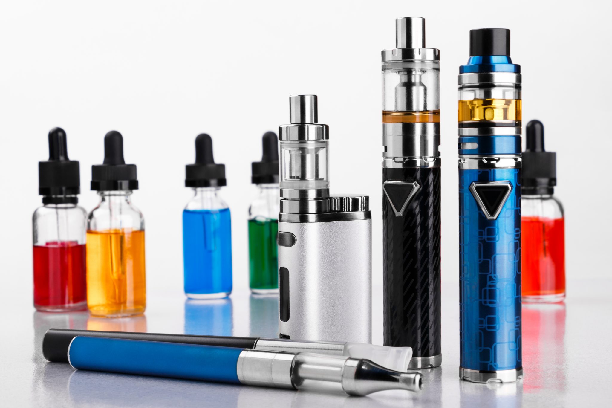 Modern electronic cigarettes and bottles with assorted vape liquid on white background