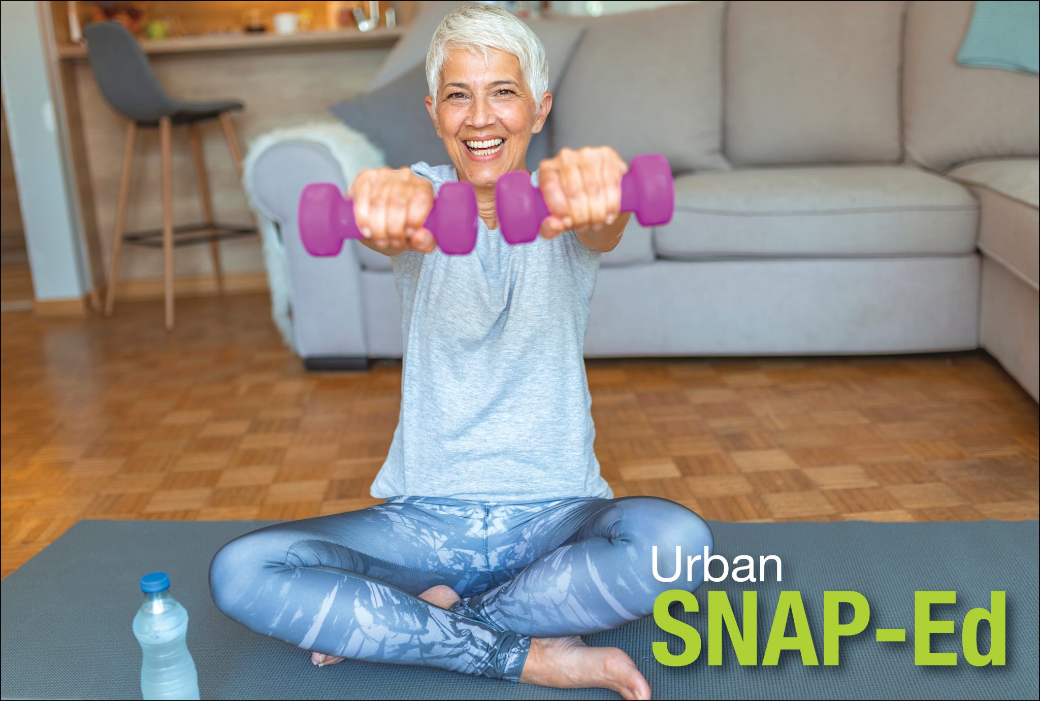 Older adult woman sitting on a yoga mat in her living room lifting hand weights. Drinking water.