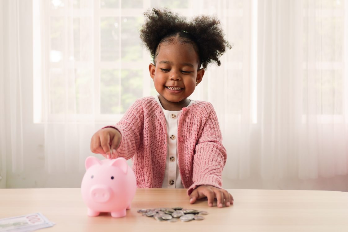 Little girl putting coin of cash into ceramic piggy bank