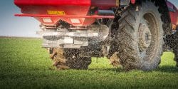 A red tractor and spreader in a filed spreading fertilizer.