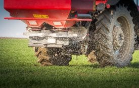 A red tractor and spreader in a filed spreading fertilizer.