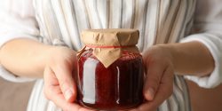 A woman holding a glass jar with strawberry jam.