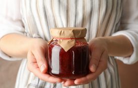 A woman holding a glass jar with strawberry jam.