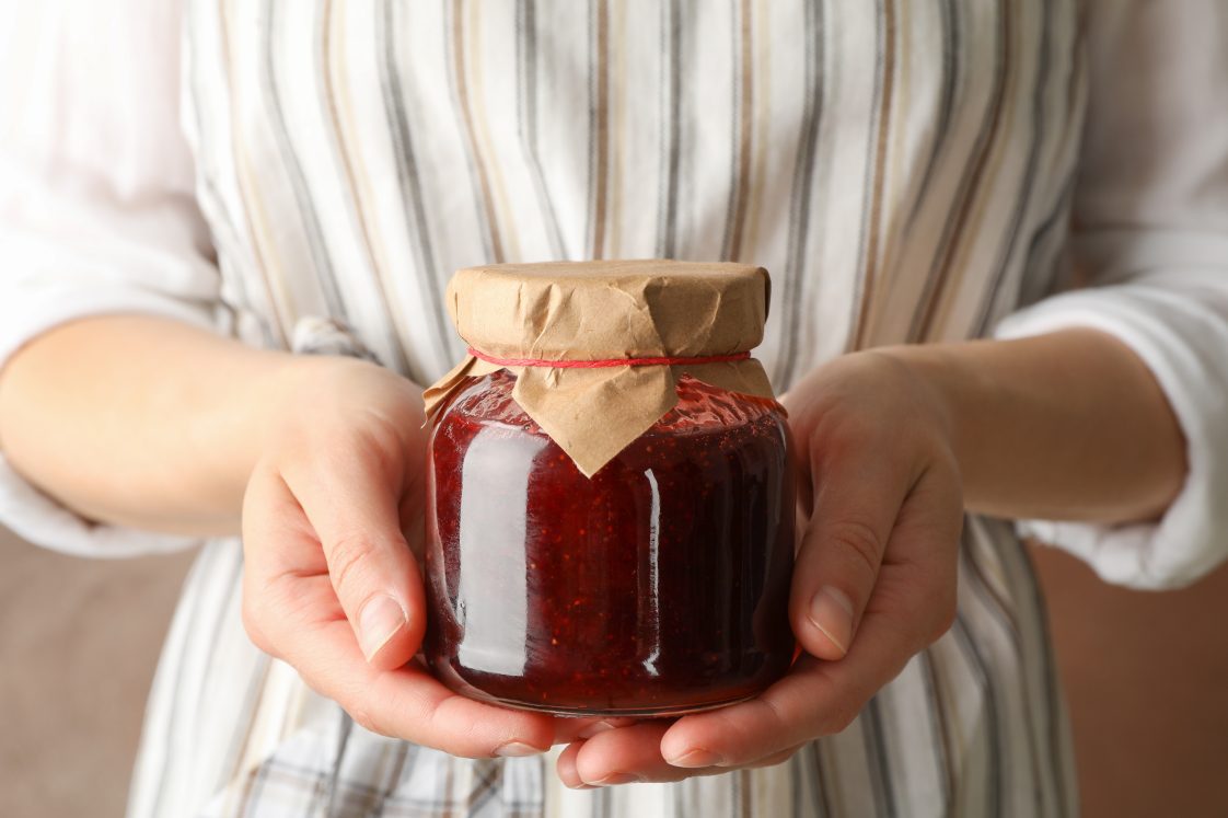 A woman holding a glass jar with strawberry jam.