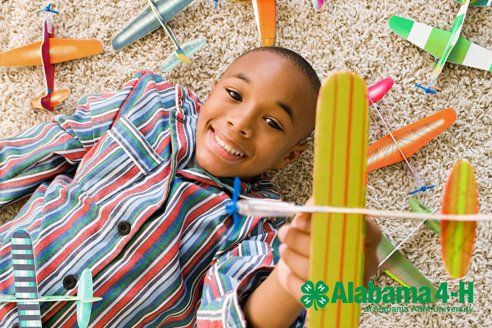 African American boy lays on the carpet playing with foam model airplanes